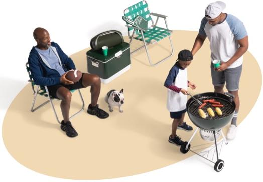 View from above of a father and son grilling hotdogs and corn on the cob as a neighbor and his dog supervise from a nearby lawn chair.